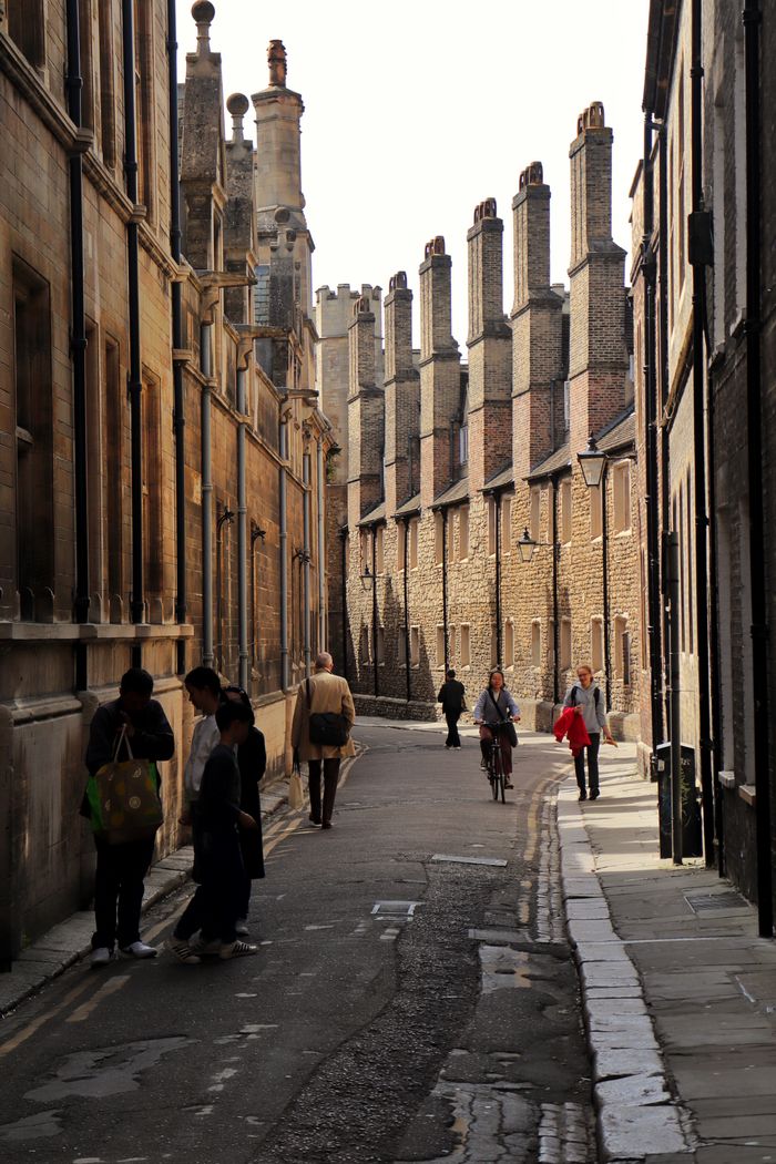 Mastering the First Impression: Your intriguing post title goes here A quaint alleyway in Cambridge with people walking and cycling, showcasing historical architecture and urban life.